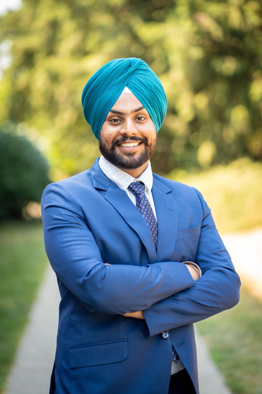 Professional portrait of person in turban and blue suit outdoors.