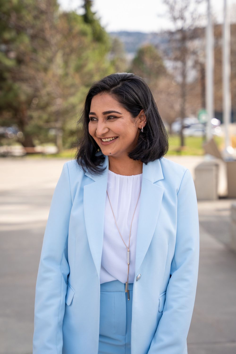 Business professional in powder blue suit and white top smiles outdoors.
