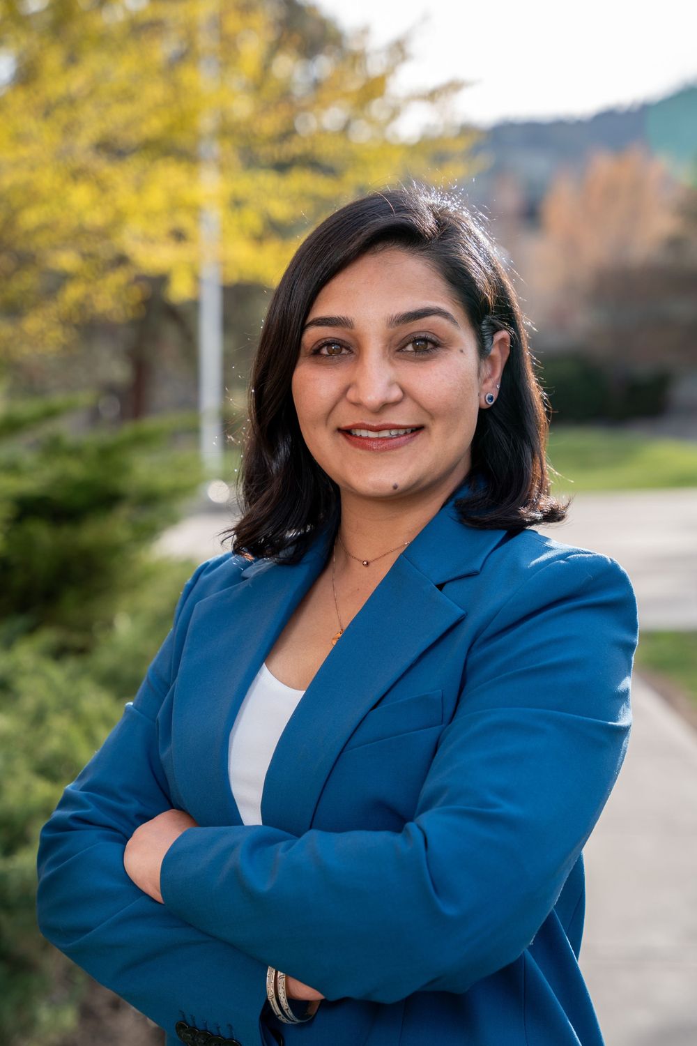 Professional wearing navy blazer and white top poses with crossed arms outdoors.