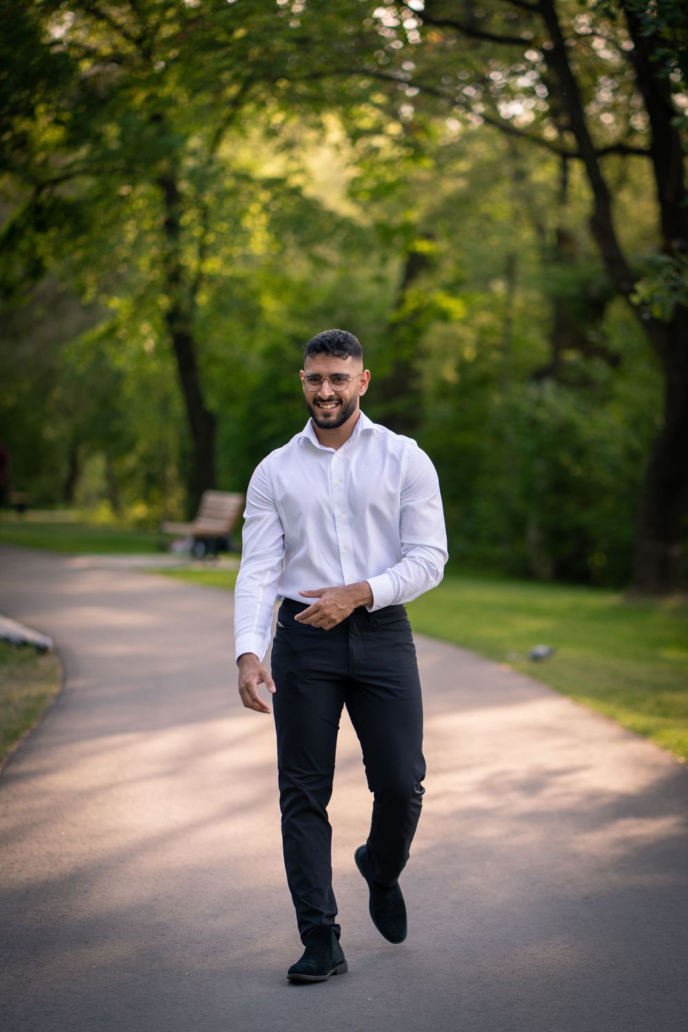 Person walking on park path in white dress shirt and black pants.