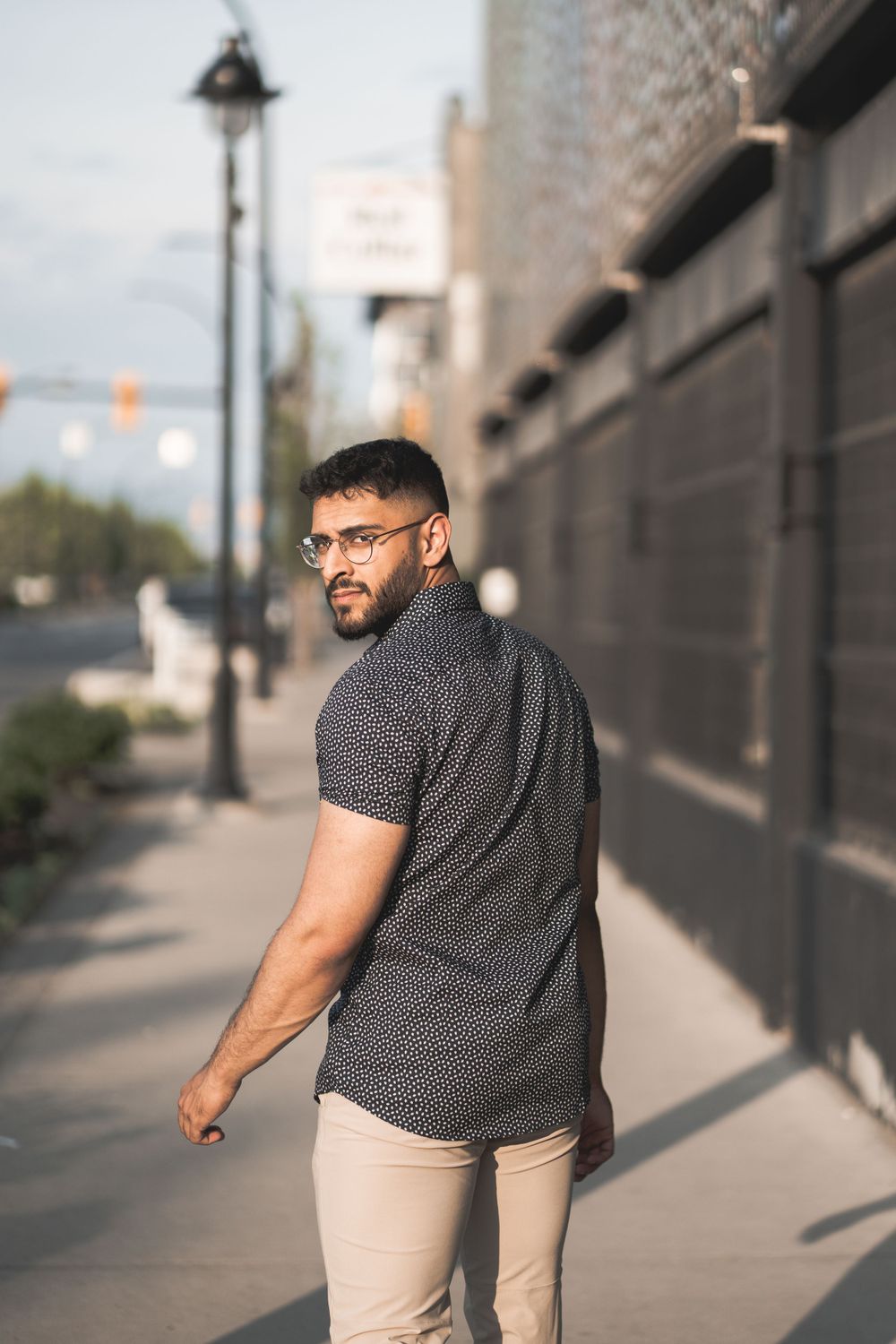 Casual urban portrait of person in patterned shirt on city sidewalk.