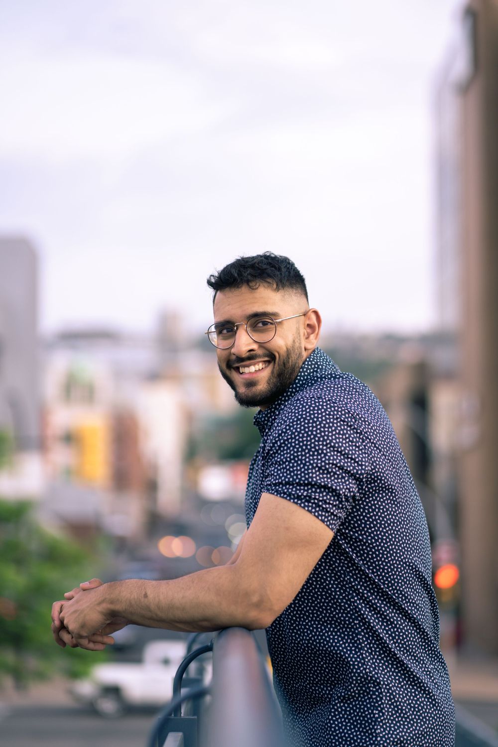 Urban portrait of person in navy polo shirt leaning on railing with city background.
