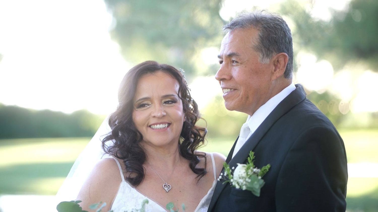 Sunny outdoor wedding photo of couple smiling at each other.