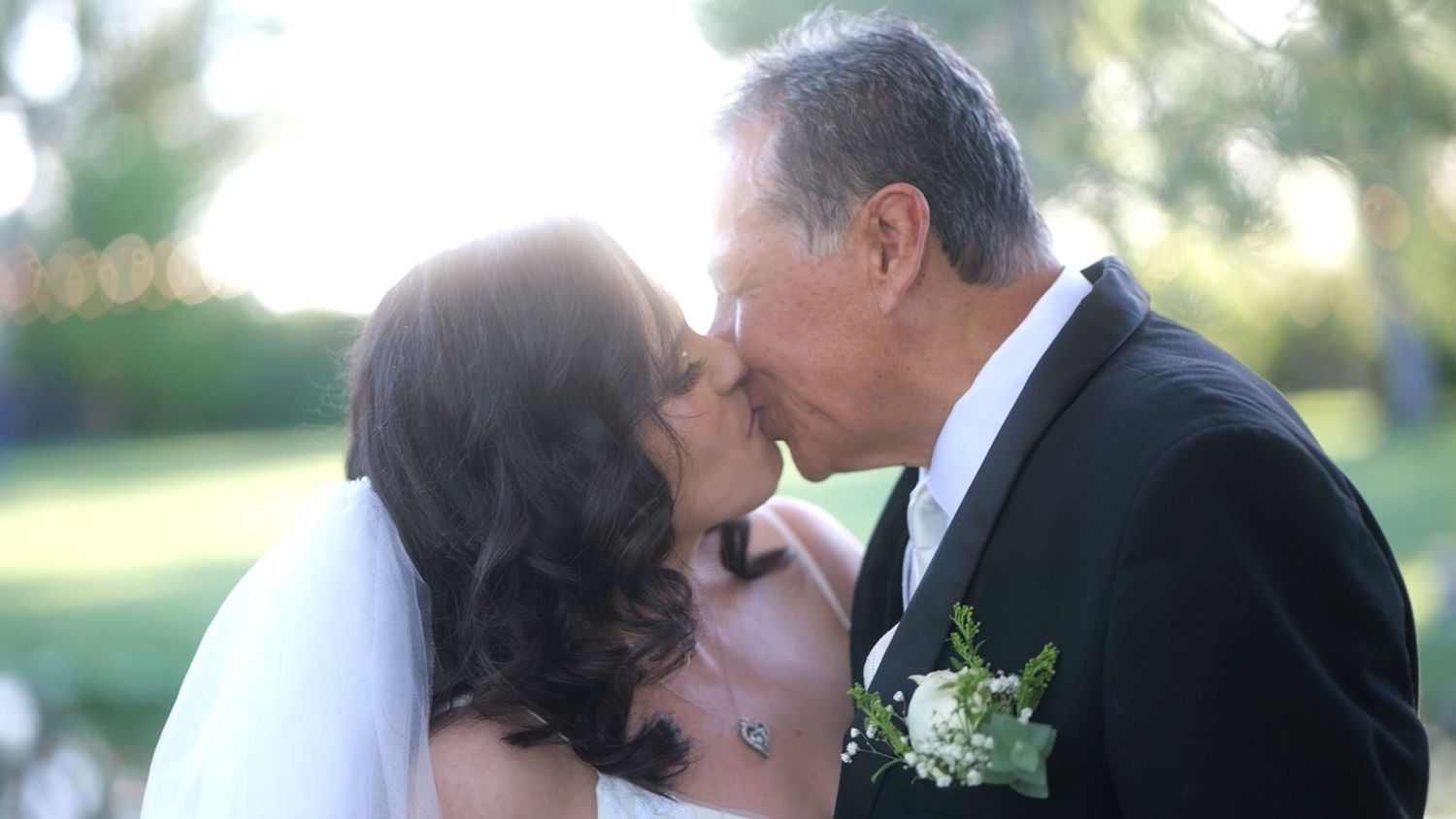 Romantic wedding kiss captured in soft outdoor lighting.