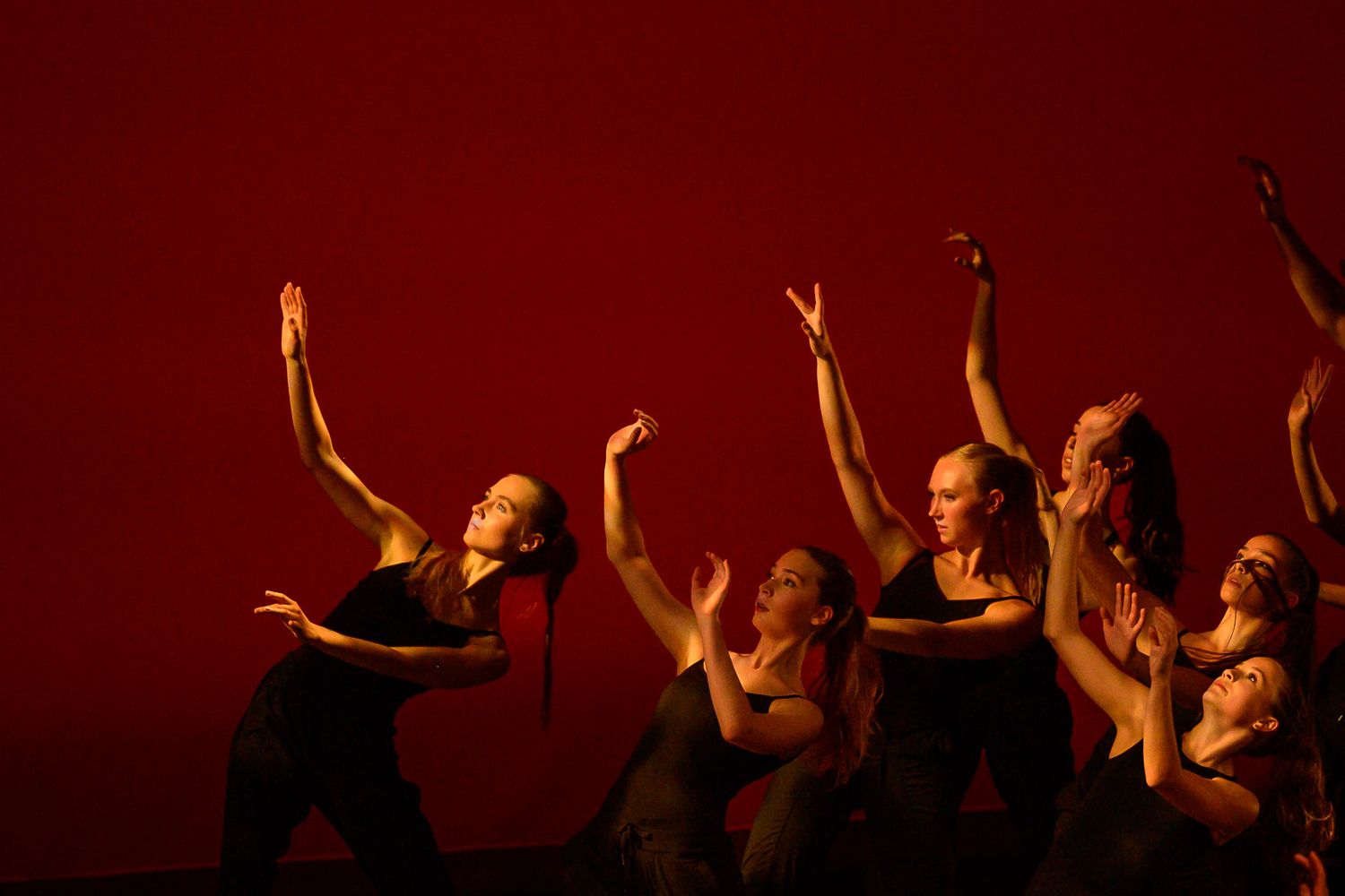 Five dancers pose in silhouette against vibrant red and orange backdrop on stage.