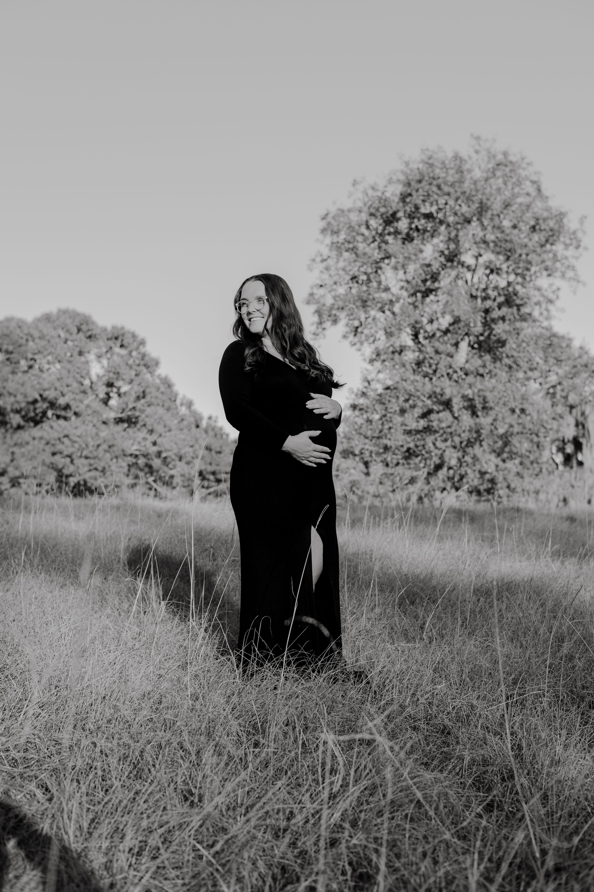Black and white photos of two figures embracing in a grassy meadow with trees in the background.