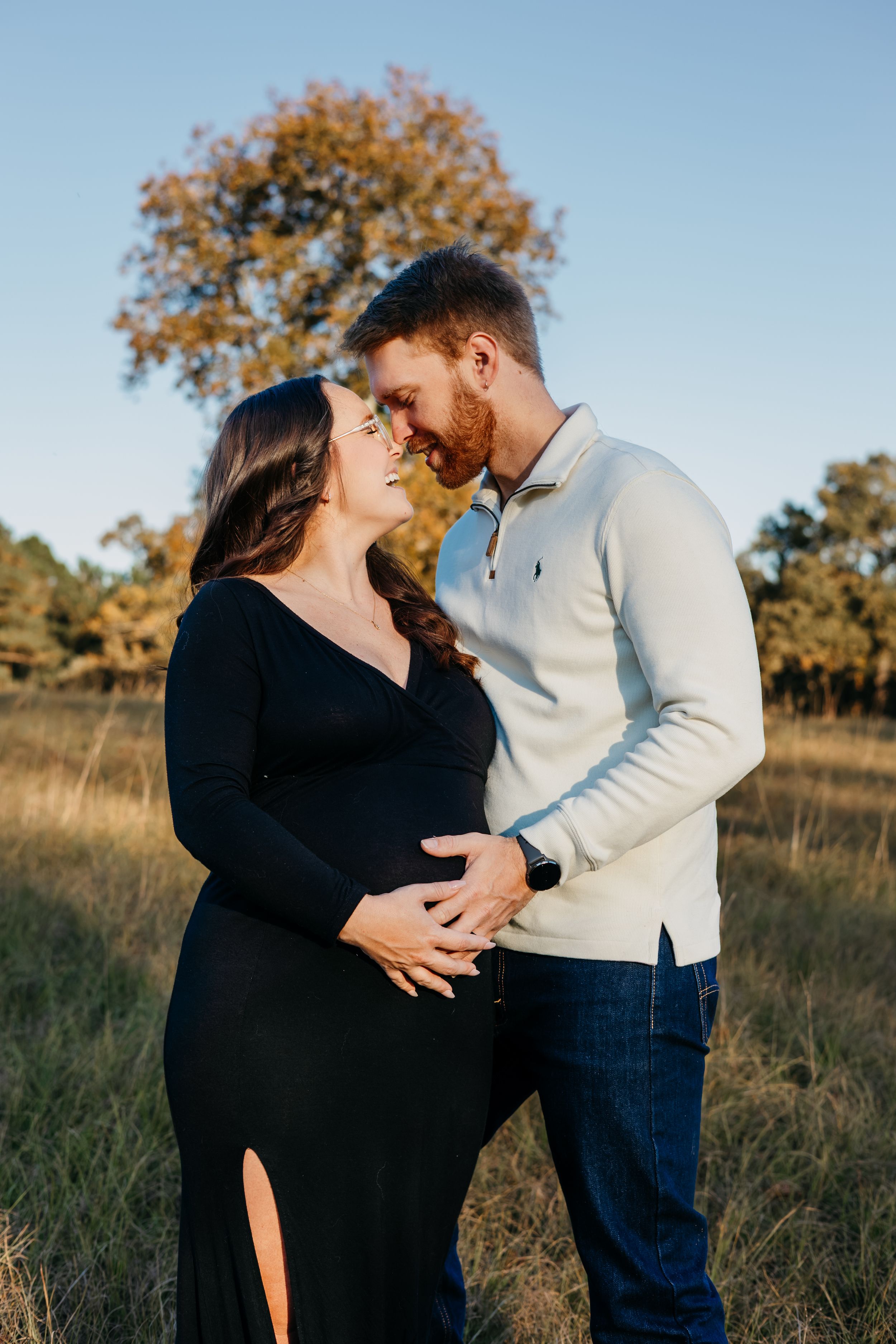 A romantic couple shares intimate moments in a field during golden hour as autumn trees glow in the background.
