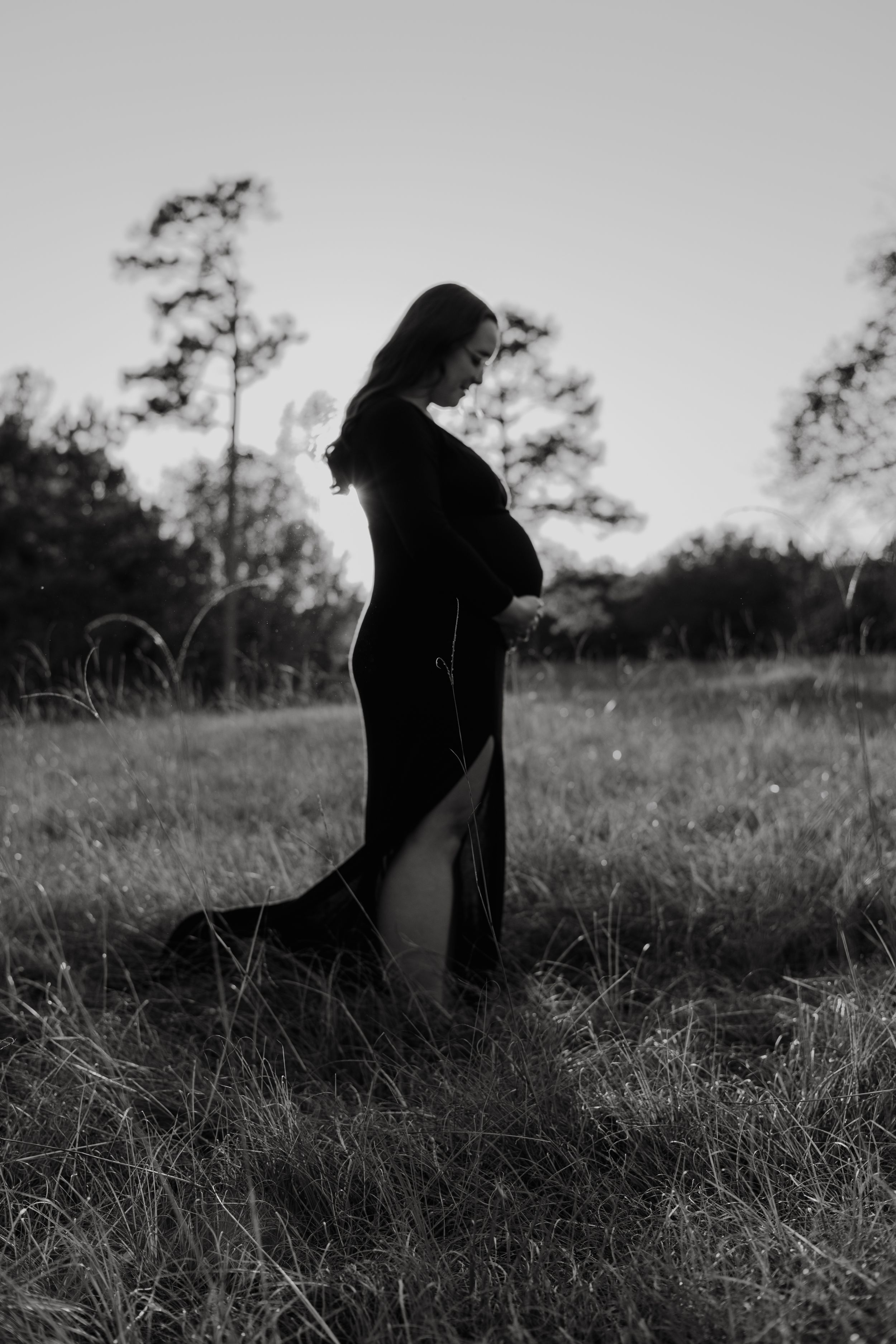 A dark silhouetted figure in a hooded cloak stands mysteriously in a grassy field against a moody black and white backdrop.