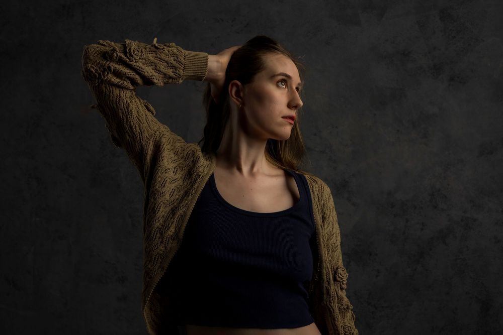 Person in dark attire poses against textured backdrop with dramatic side lighting creating moody ambiance.
