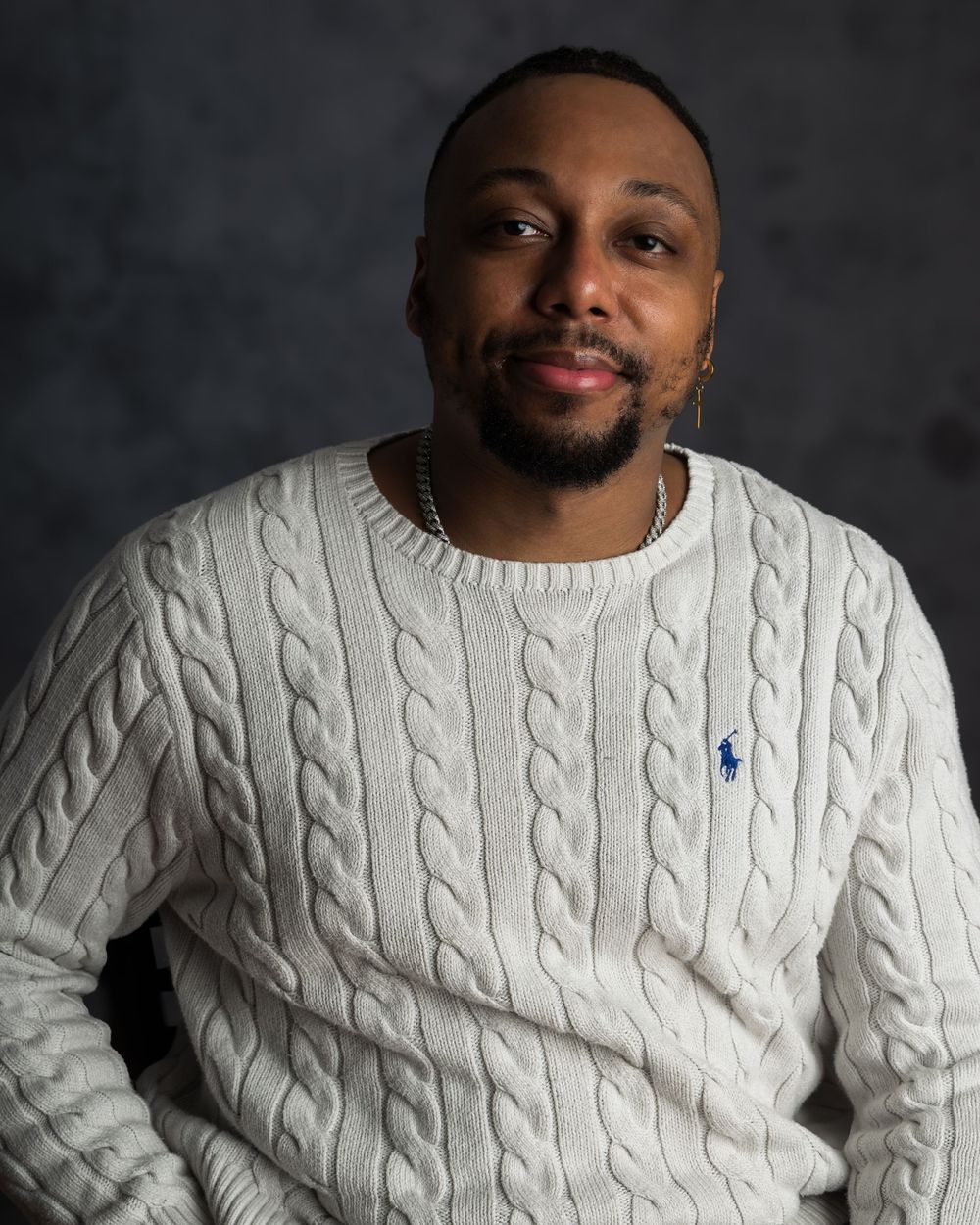 Person wearing a white cable-knit sweater with navy accent detail poses against dark background.