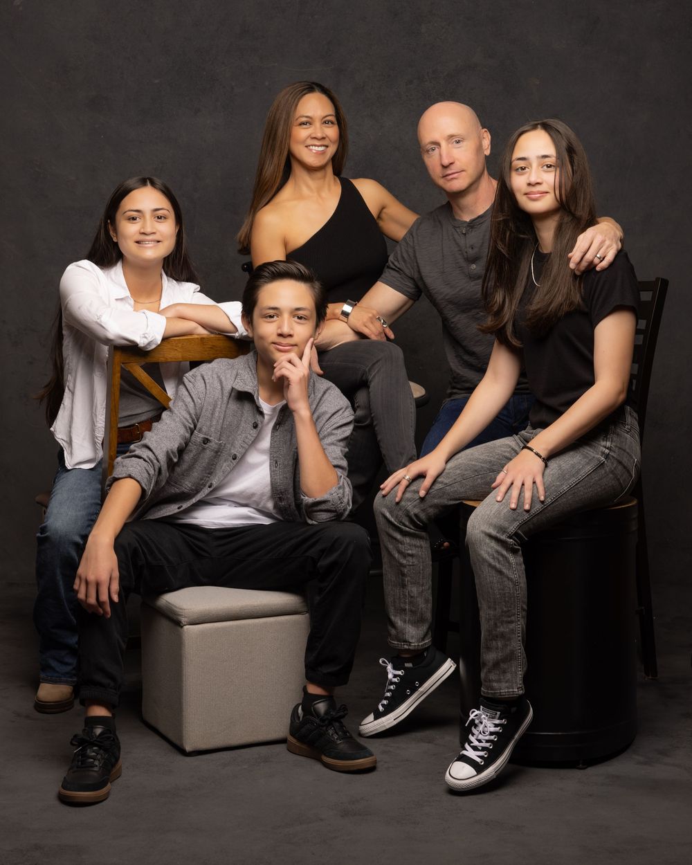 Professional studio portrait of group in casual attire sitting together against dark background.