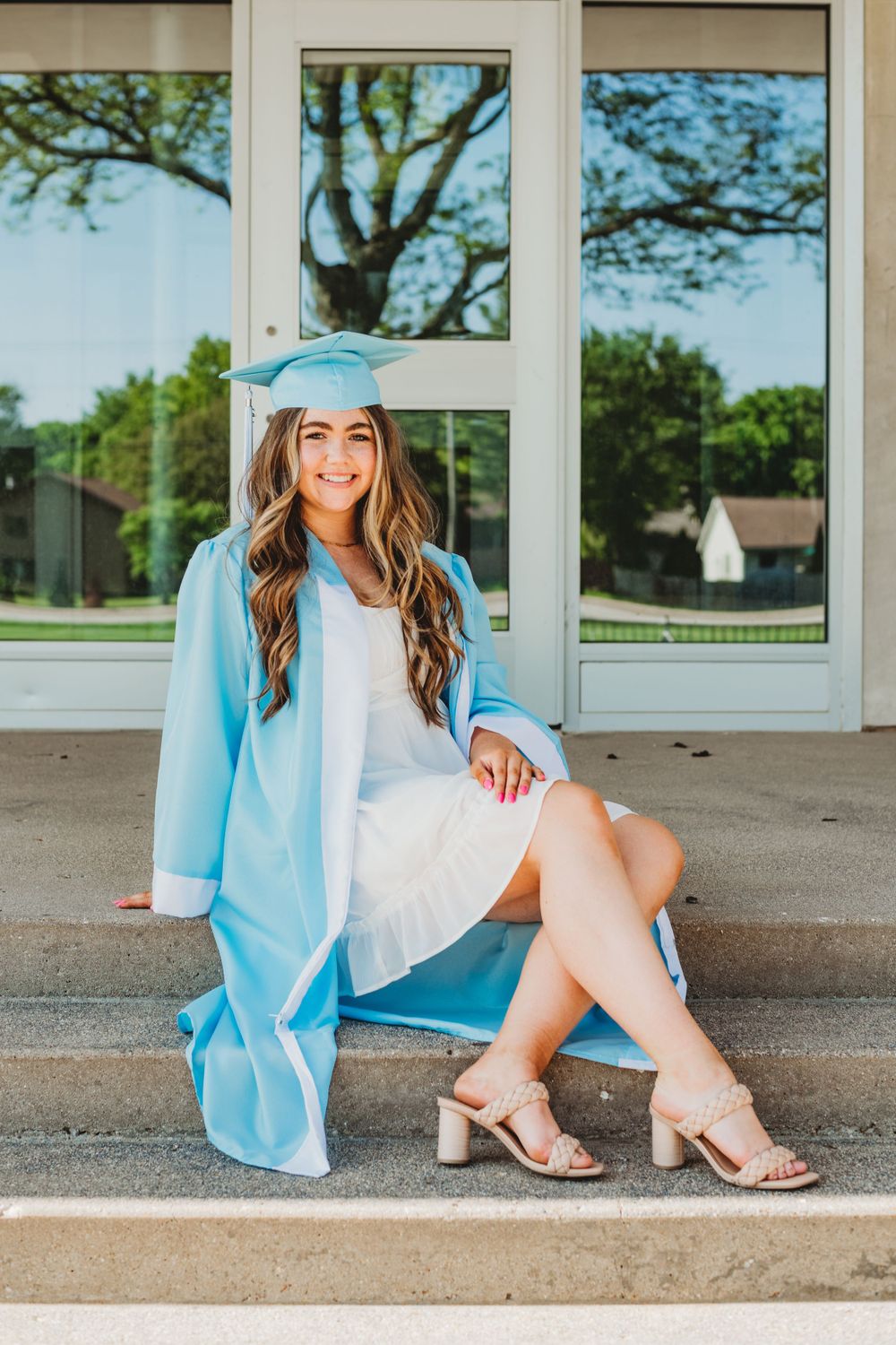 Graduate in blue graduation gown sitting on school building steps.