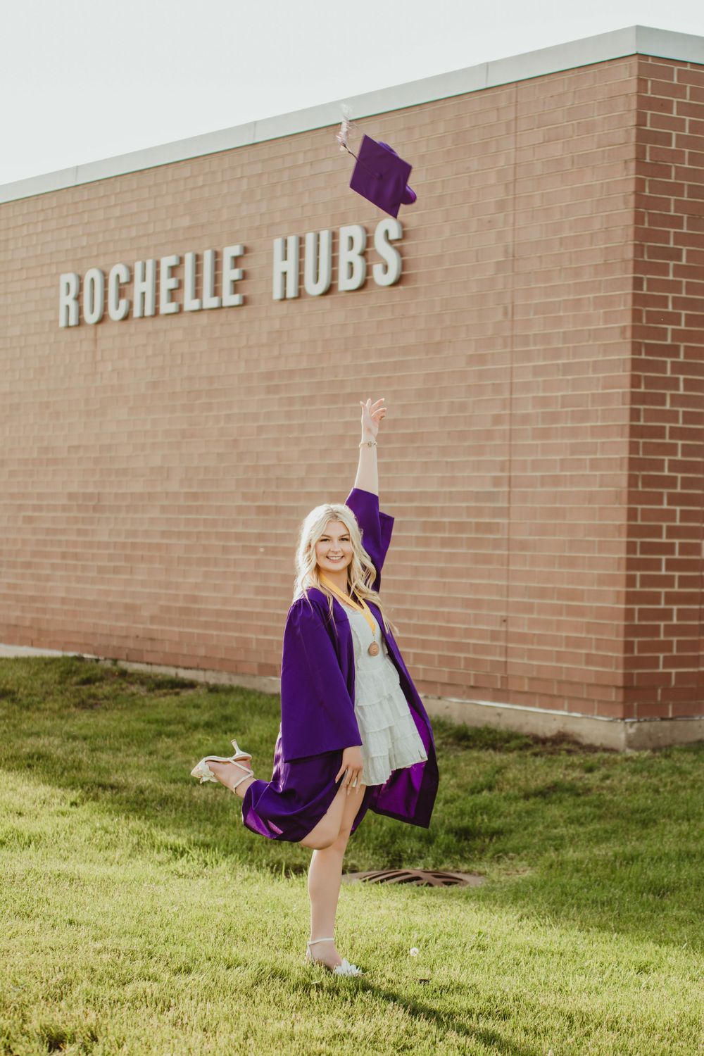 Graduate tossing purple cap in front of brick school building.