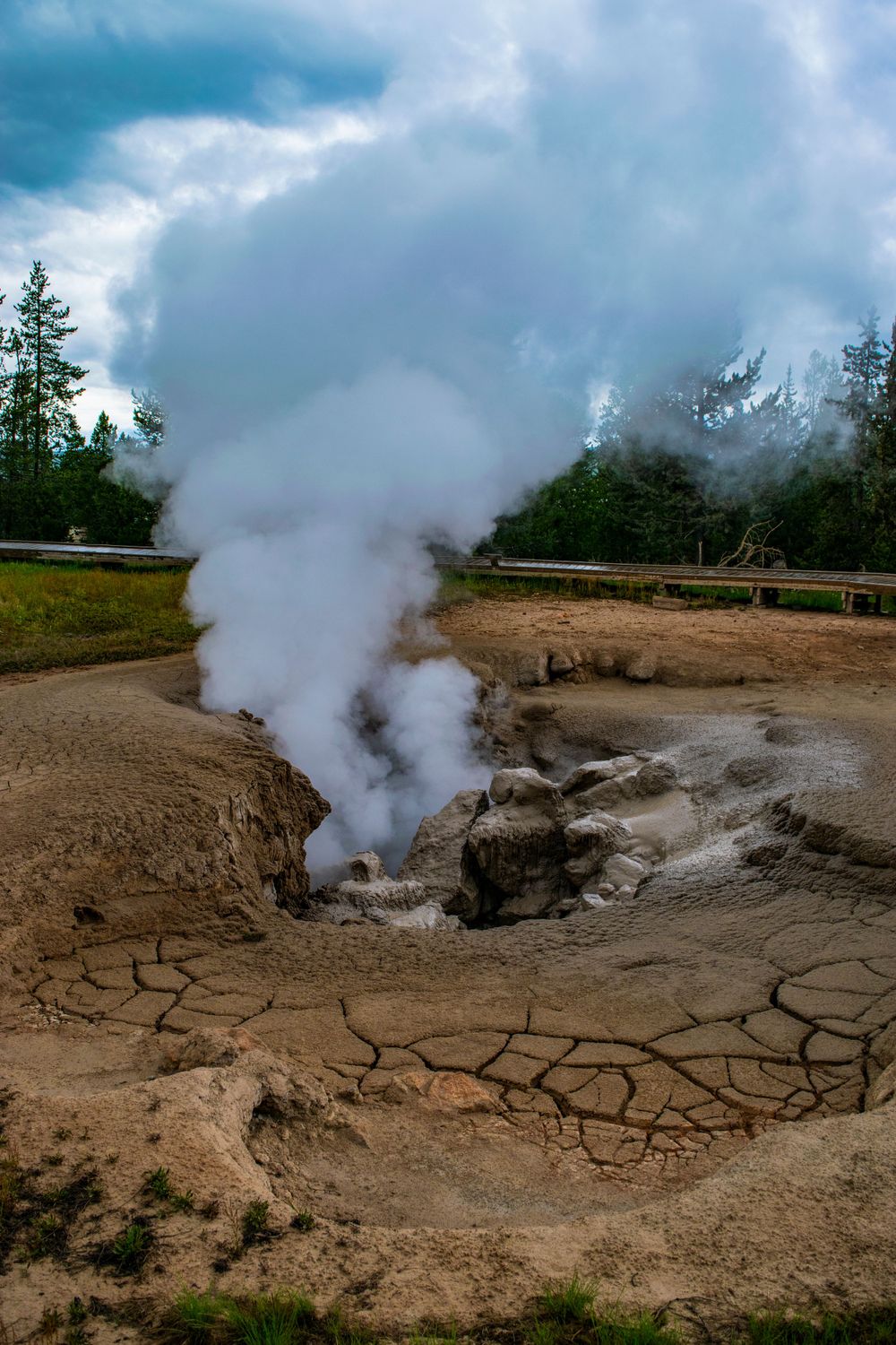 Steam rises dramatically from a cracked mud geyser crater in a geothermal landscape.