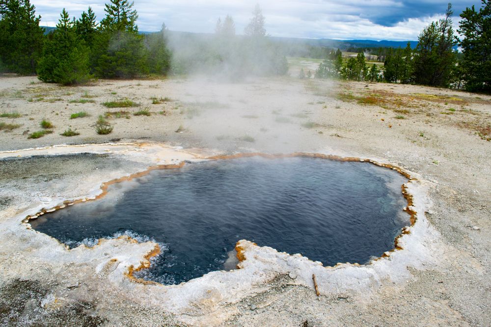 Dark blue hot spring with orange mineral deposits around its edges in volcanic terrain.