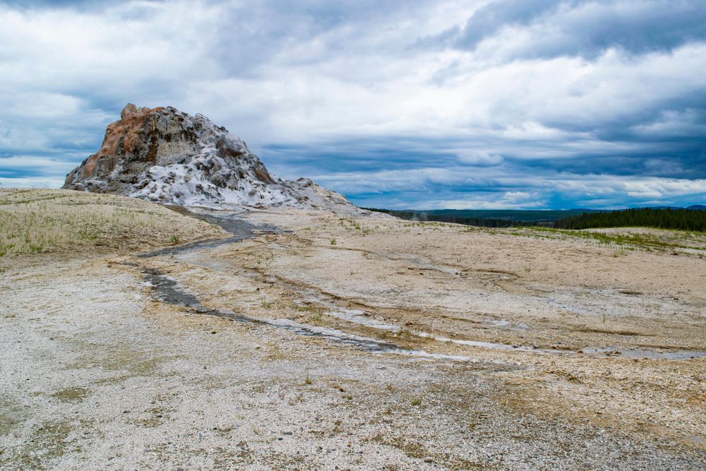 A rocky mound formation rises from a barren landscape under dramatic cloudy skies in Yellowstone National Park.