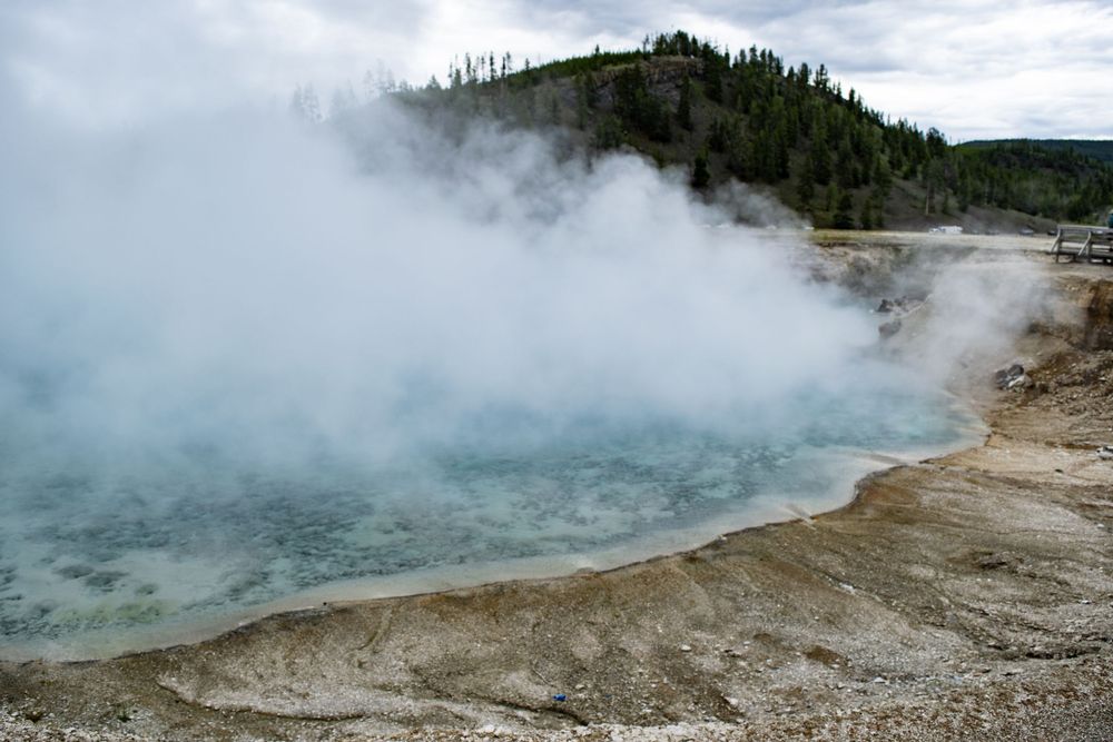 Steaming turquoise geothermal pool surrounded by mineral deposits in a volcanic landscape.