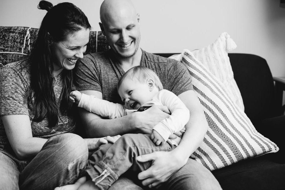Intimate black and white family portrait showing natural interactions and smiles on a sofa.