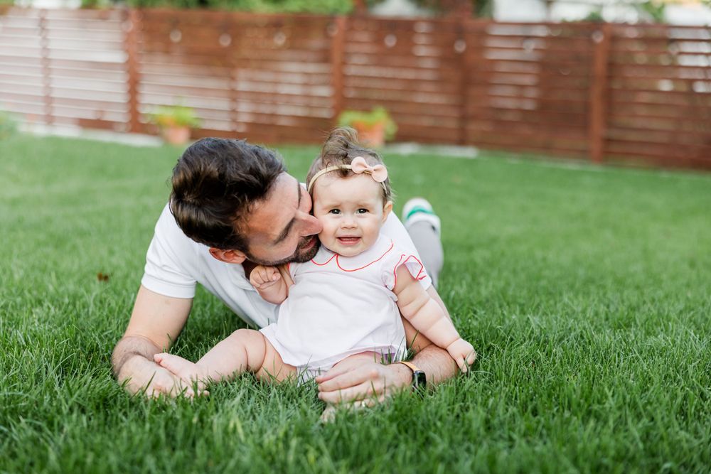 Family enjoying a playful moment together on lush green grass during a sunny outdoor photo session.