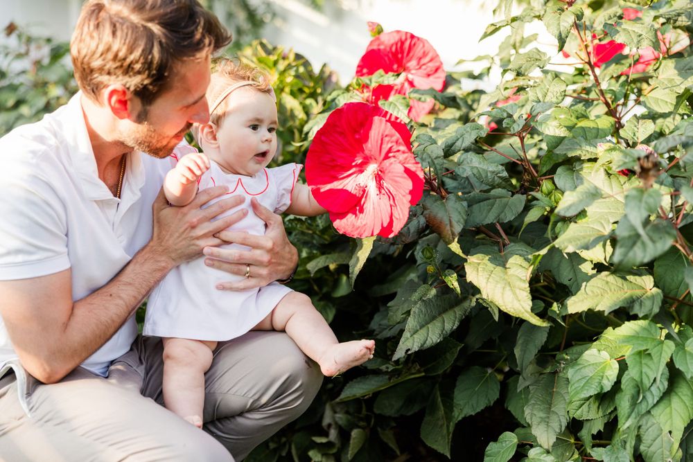 Family photo session among vibrant red flowers and green foliage in a garden setting.