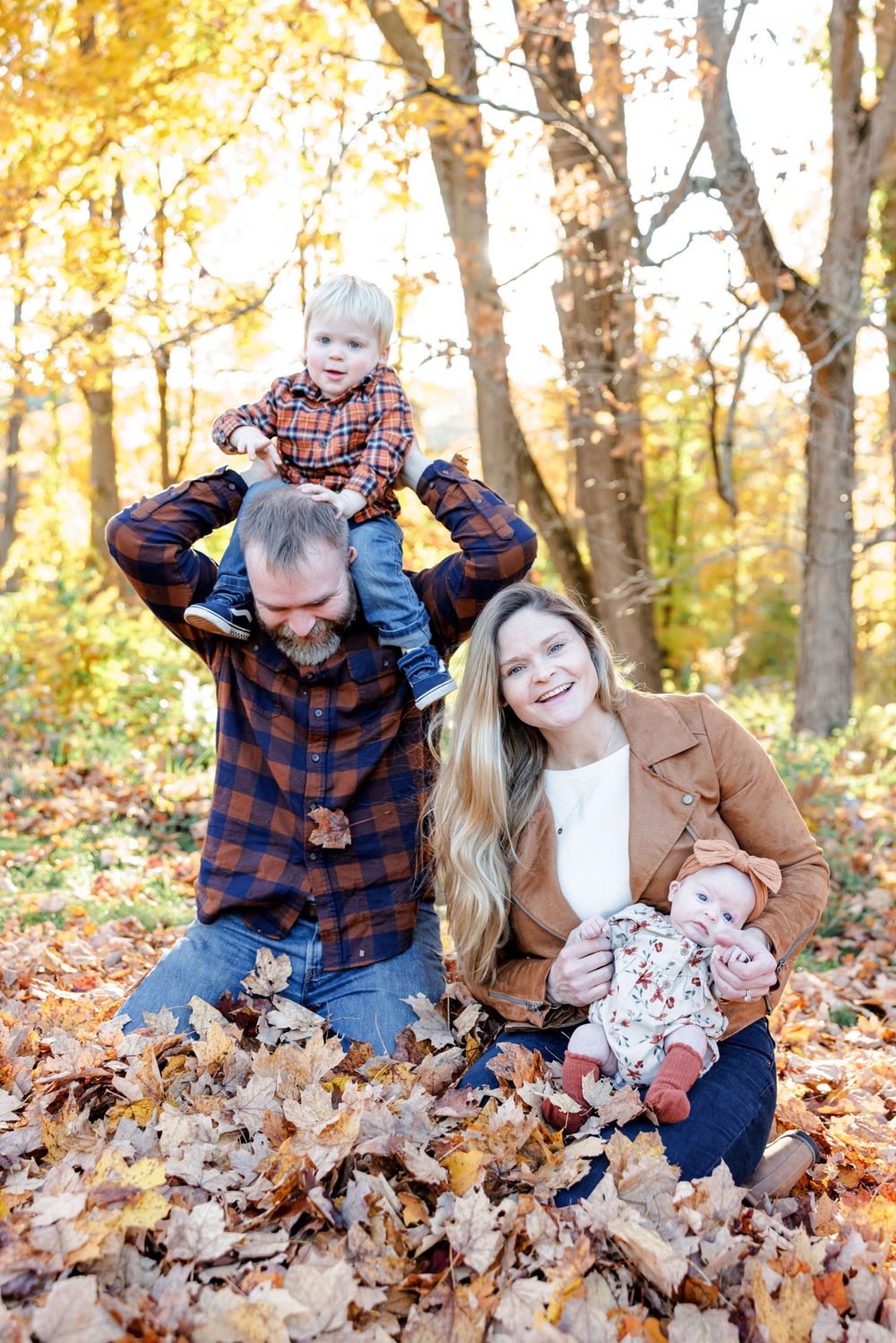 A family enjoys a playful autumn moment together among fallen leaves in a sunlit forest.
