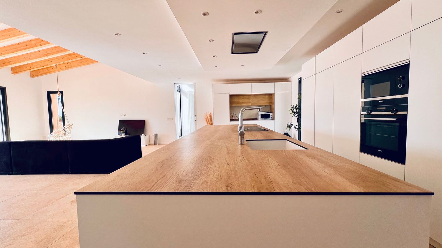 Spacious modern kitchen interior with long wooden island and white cabinetry under recessed lighting.