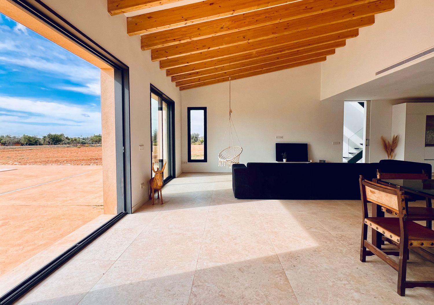 Modern living room with wooden beam ceiling and large windows overlooking desert landscape.