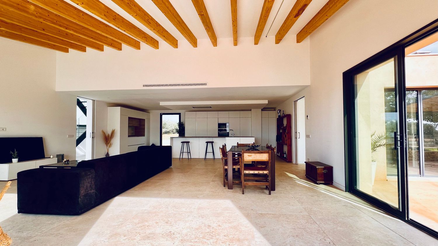 Spacious open-concept living area with wooden beam ceiling and sliding glass doors.
