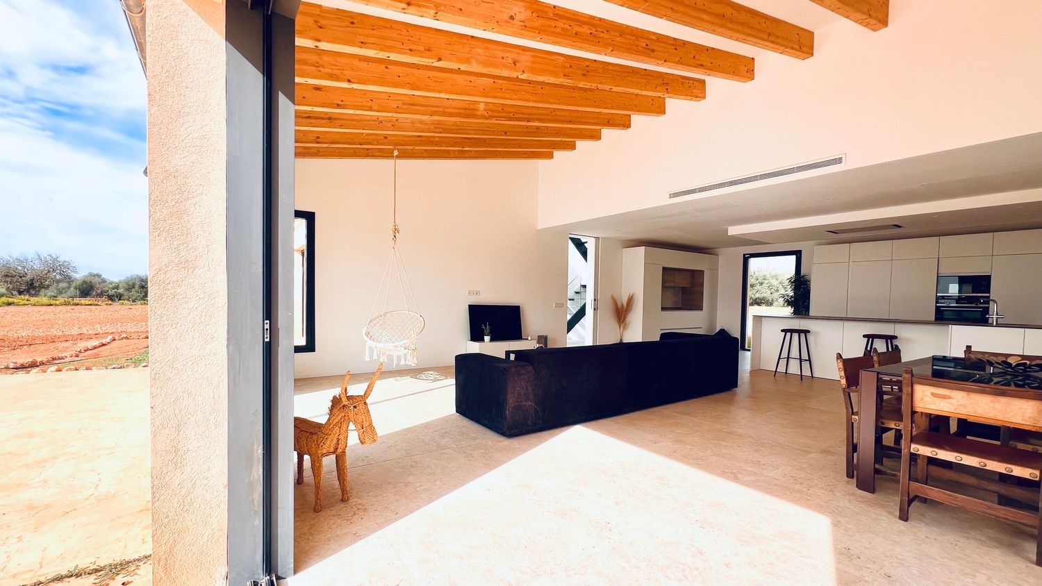 Modern open-plan interior with exposed wooden beams and large sliding doors opening to exterior.