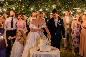 Wedding cake cutting ceremony under twinkling lights at outdoor evening reception.