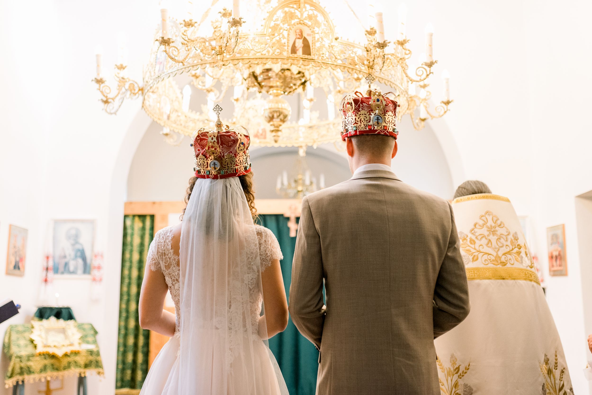 Wedding ceremony in ornate church with chandelier and golden altar decorations.