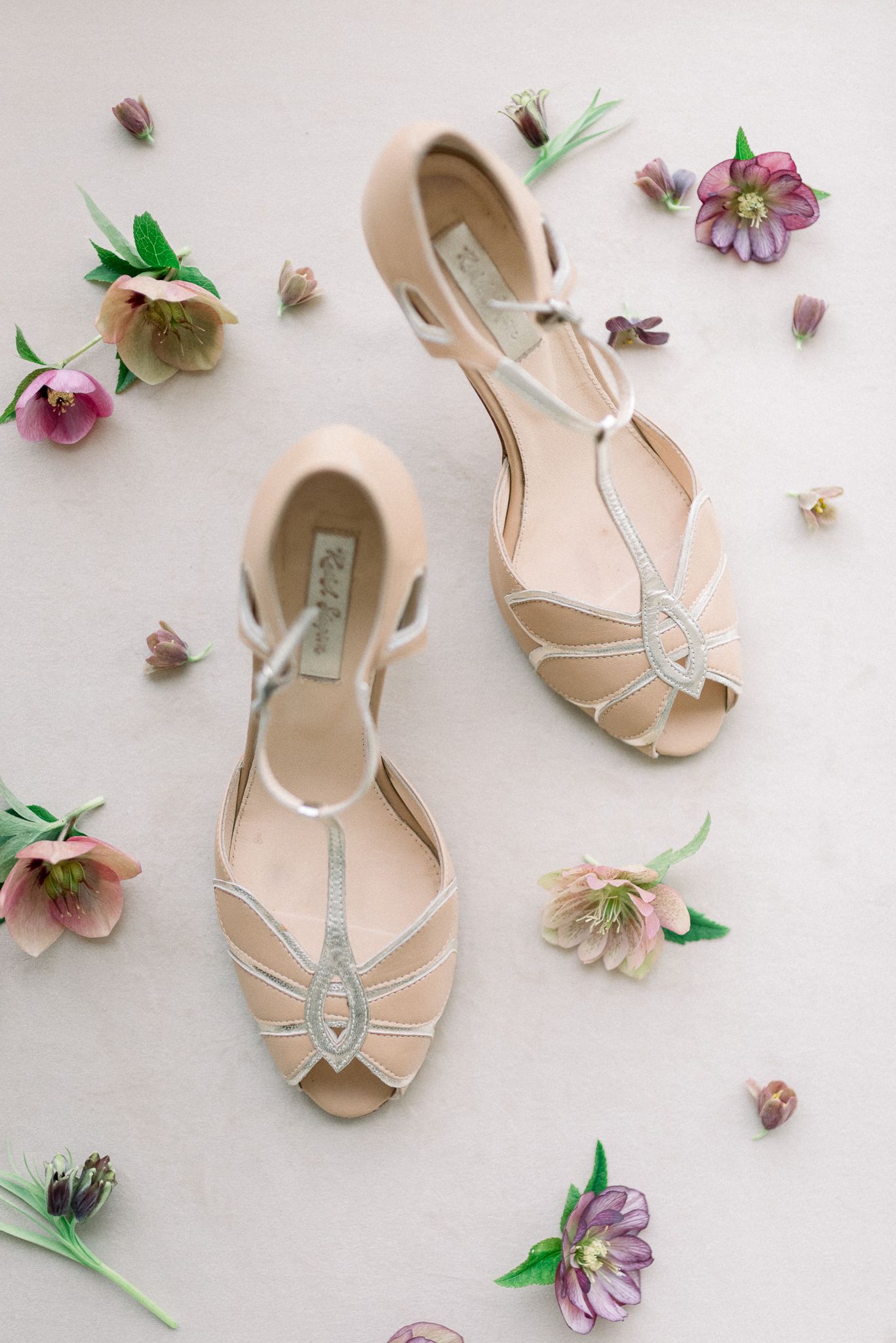 Vintage-style blush wedding shoes surrounded by delicate pink hellebore flowers.