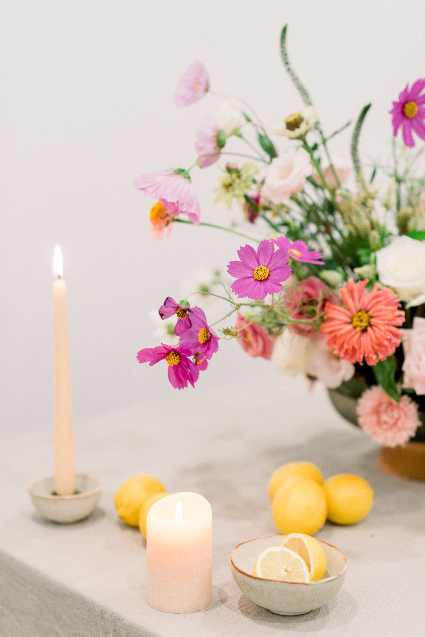Romantic table setting with pink cosmos flowers, lit candles and fresh lemons on linen tablecloth.