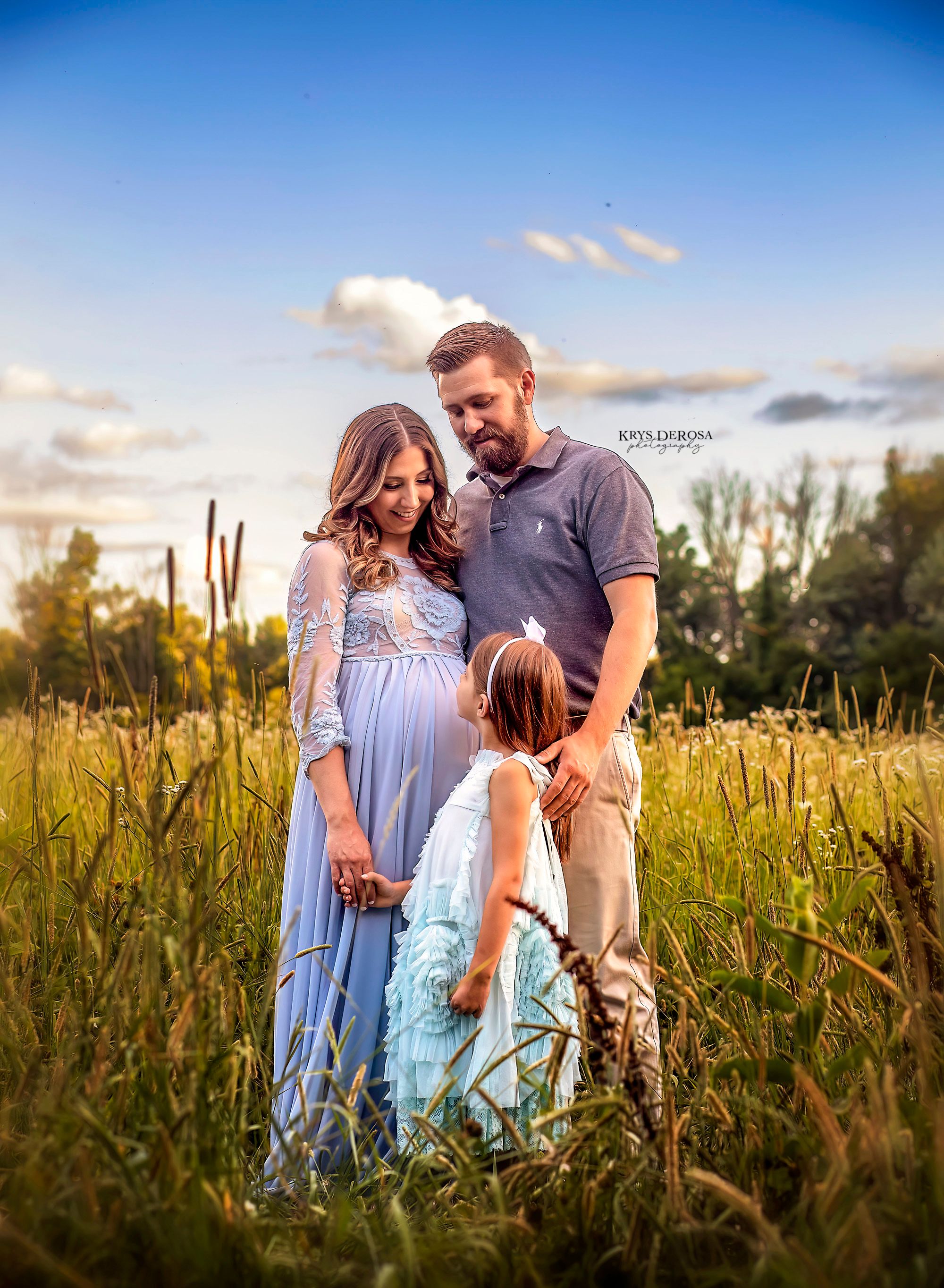 A family shares tender moments together in a golden sunlit meadow during sunset, wearing coordinated blue outfits.