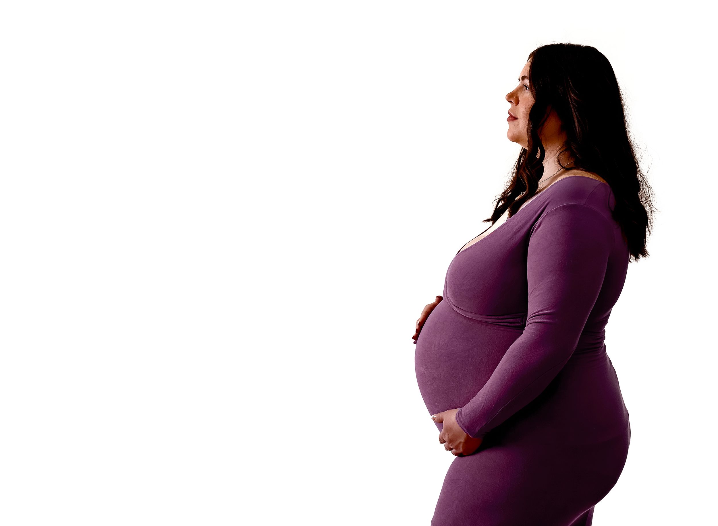 Pregnant woman in purple dress cradling her baby bump, side profile view on white background.