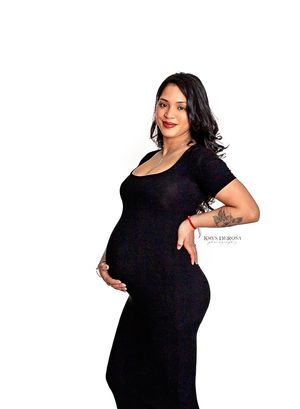 Pregnant woman in black dress cradling baby bump during professional maternity photo shoot on white background.