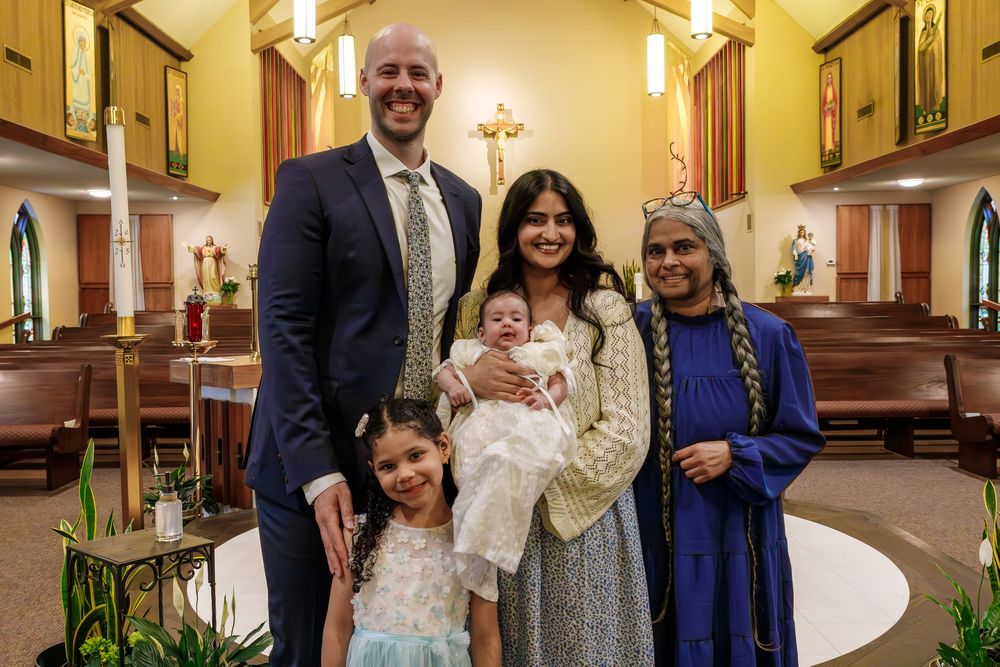 Family gathering inside a church during a baptism ceremony with adults and children dressed in formal attire.