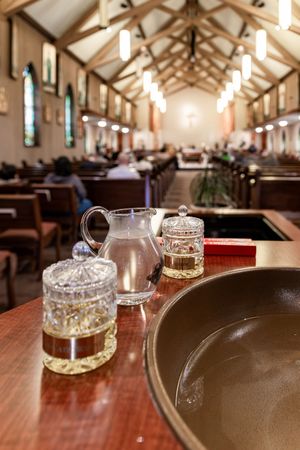 Glass jugs and vessels on wooden table inside a church sanctuary with exposed wooden beams and stained glass windows.