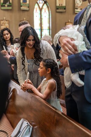 People gather in a church for a christening ceremony as they watch a baby's baptism near stained glass windows.