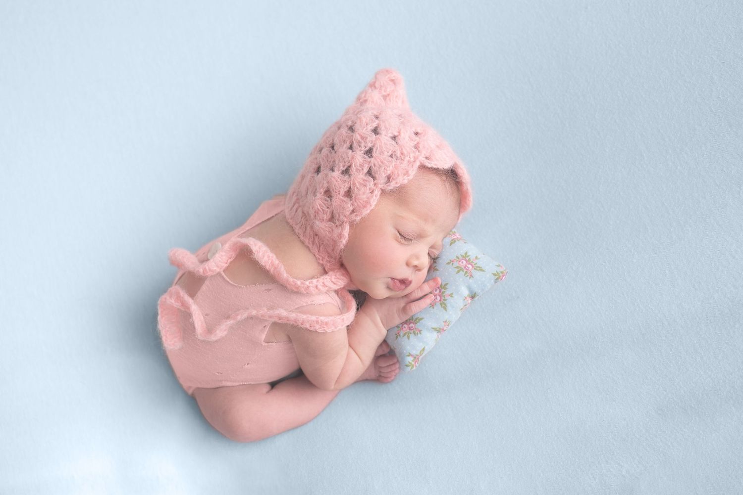 Close-up photographs of a sleeping newborn in soft pink tones on white blankets.