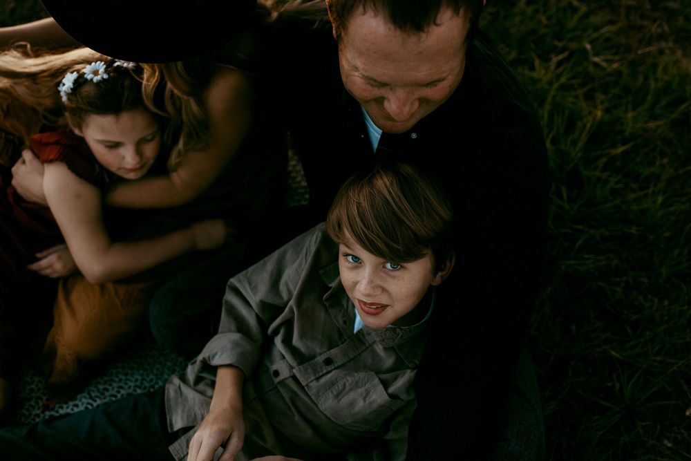 Moody dark portrait of a family sitting together in shadow against greenery background.