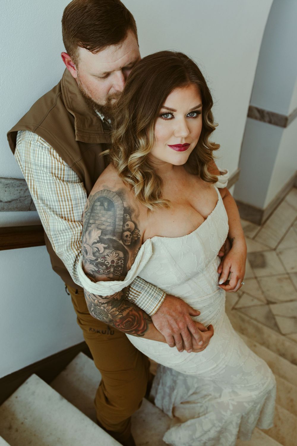 Close embrace between couple in formal attire with white lace dress and checkered blazer against light wall.