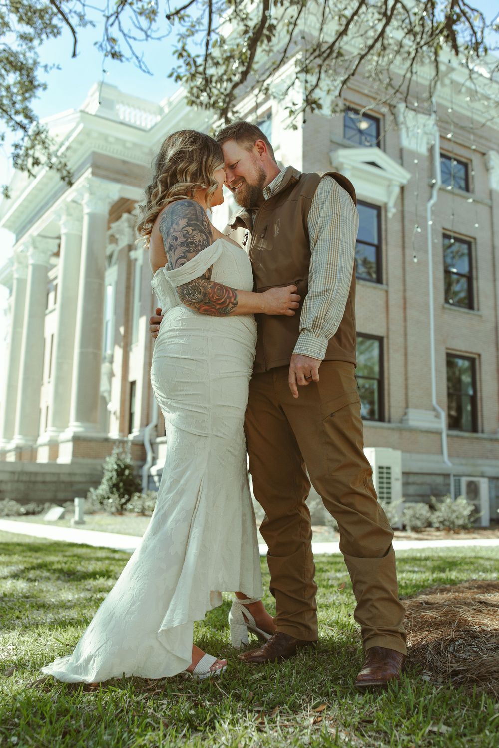 Romantic wedding series showing newlyweds in vintage-style attire embracing on the grounds of a grand historic building.