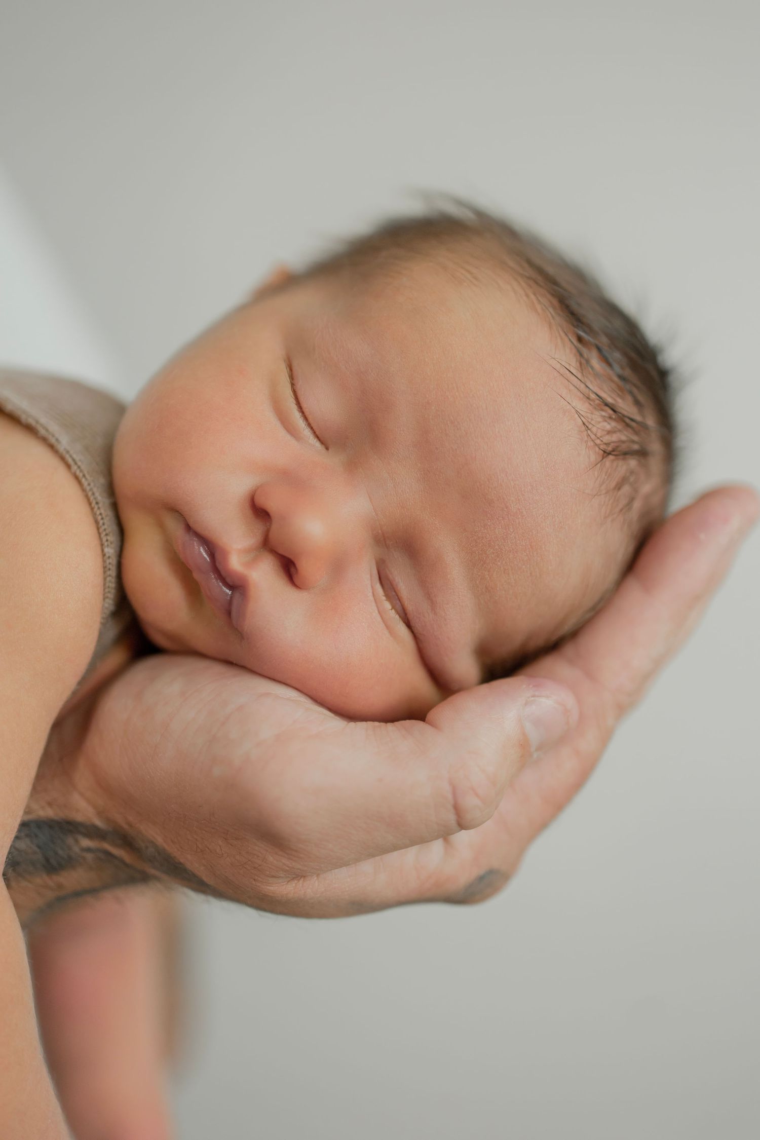 Sleeping newborn baby rests peacefully in a tattooed dads cupped hand.