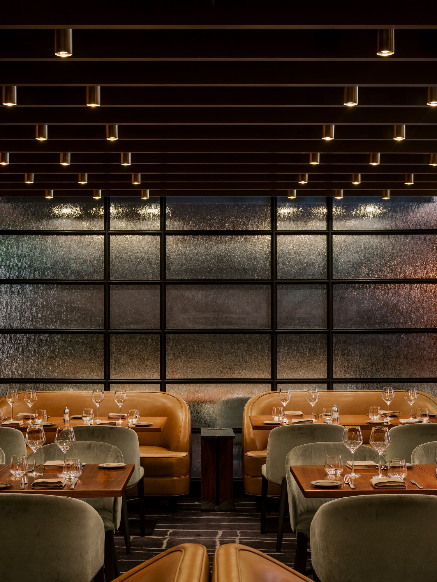 Modern upscale restaurant interior with leather booths, wood tables, and dramatic ceiling lighting creates intimate dining atmosphere.