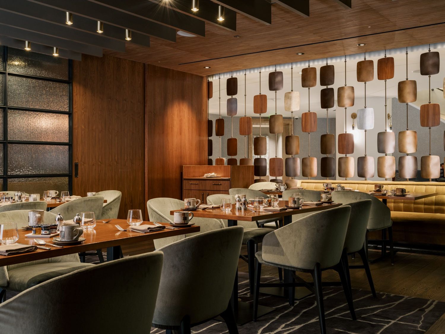 Modern restaurant dining room with geometric wall panels, leather banquette seating, and contemporary pendant lighting.