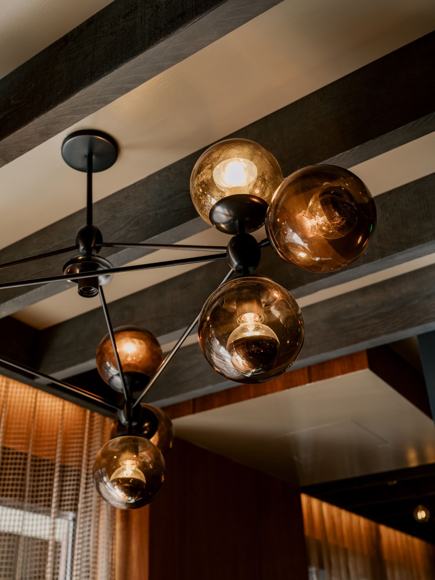 Modern ceiling light fixture with multiple amber glass globe shades mounted on black metal arms under exposed wooden beams.