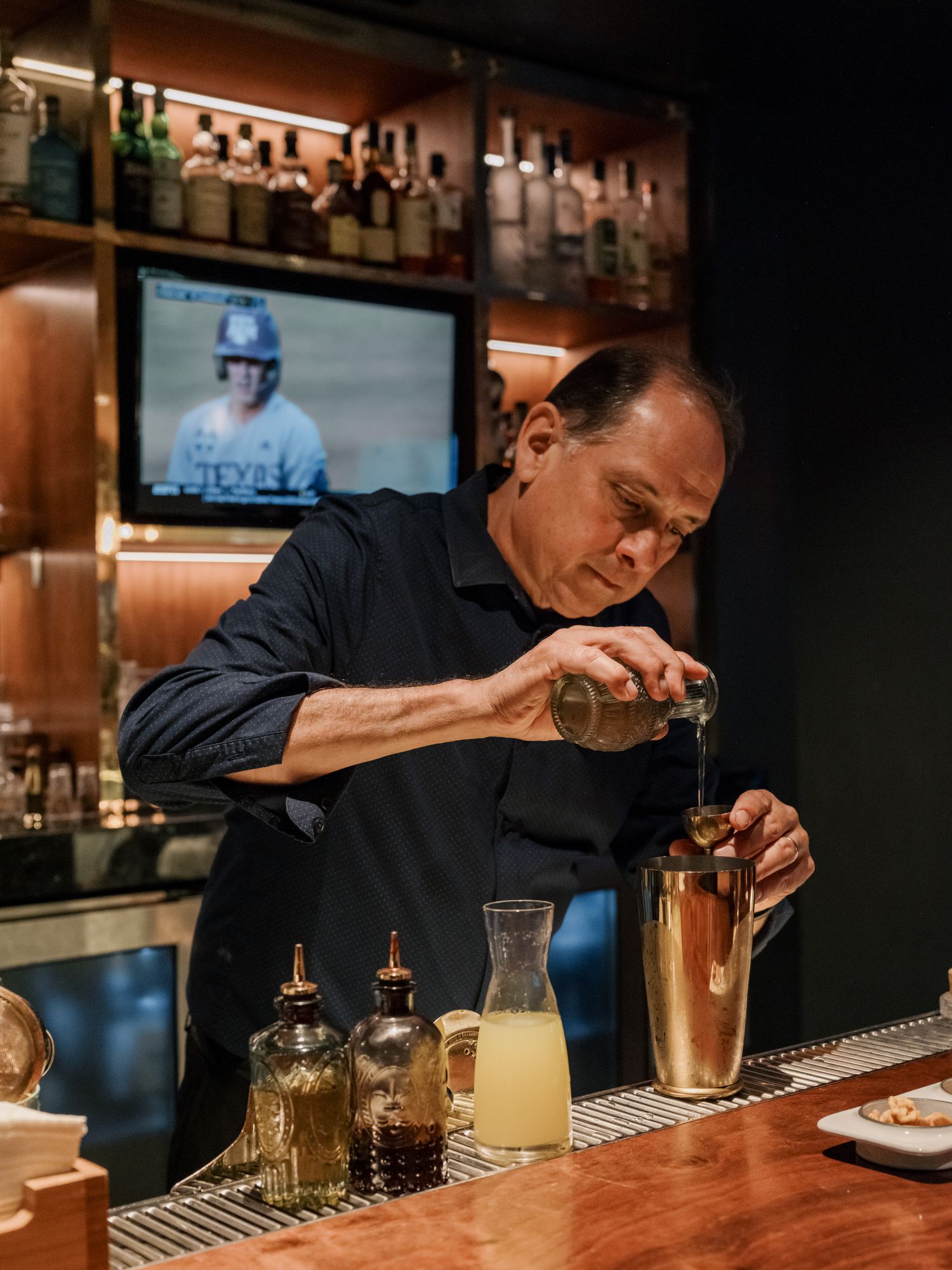 Professional bartender carefully crafting a cocktail at an upscale bar with bottles displayed in the background.