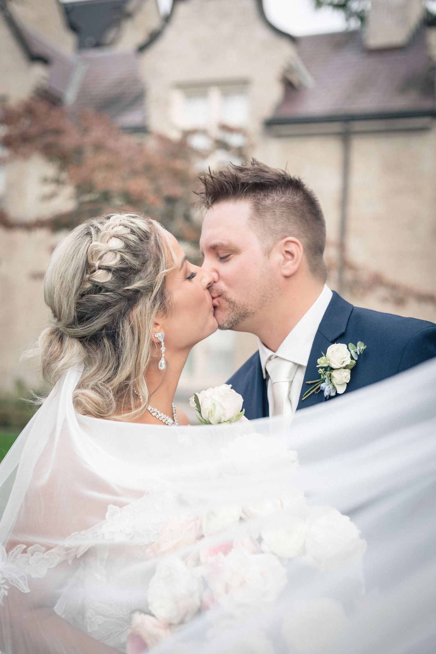Romantic wedding couple sharing a kiss under flowing white veil.
