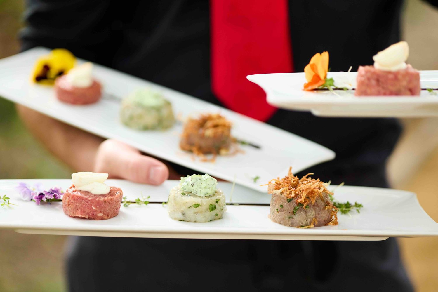 Elegant sashimi platter arranged in a row on white plates with garnishes and sauces.